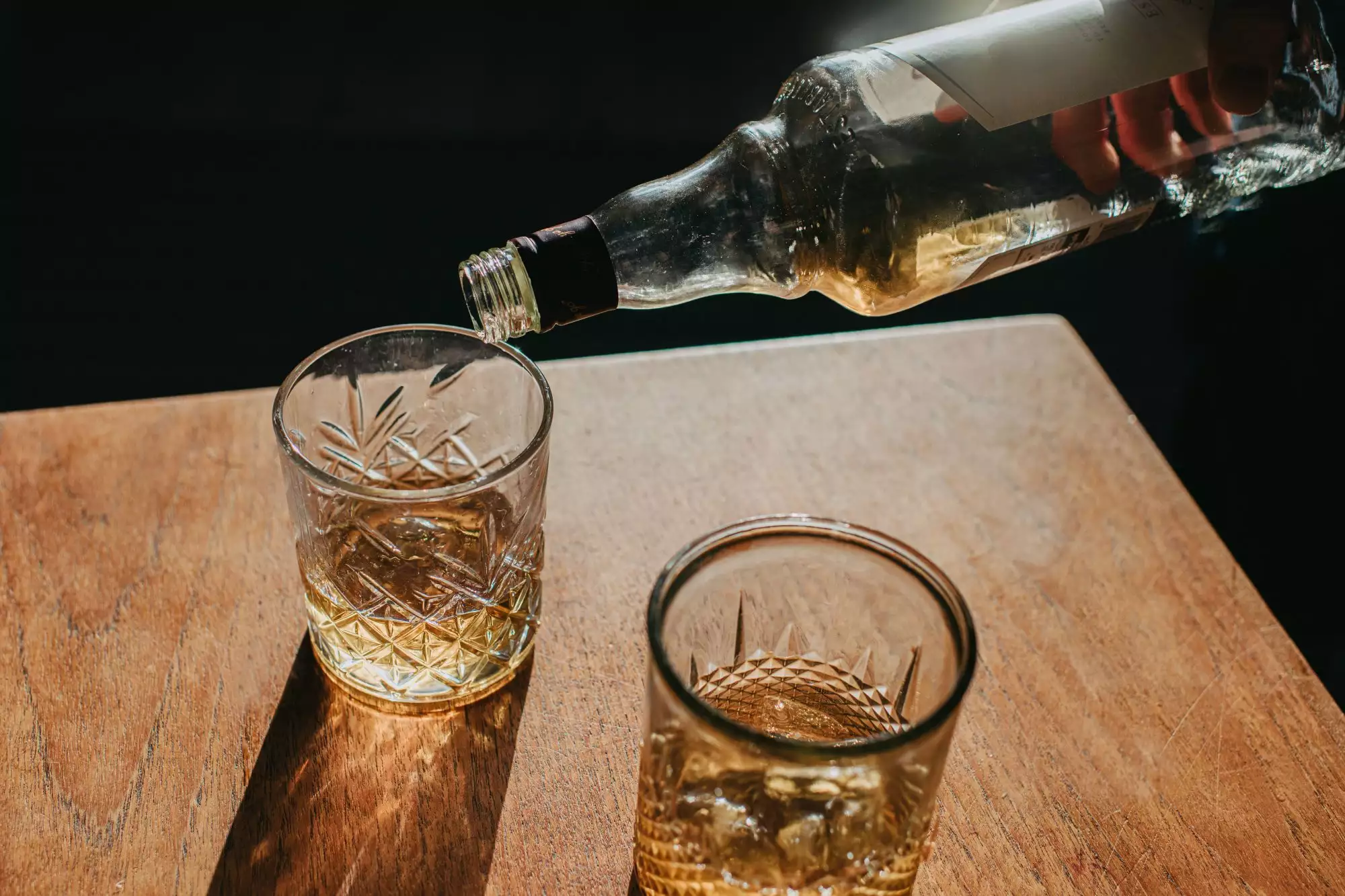 A photo of a hand pouring scotch whisky into two glasses